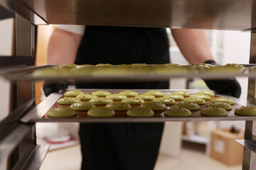 Chef placing a tray full of colorful macarons on a metal shelf with another macaroons, situated in...