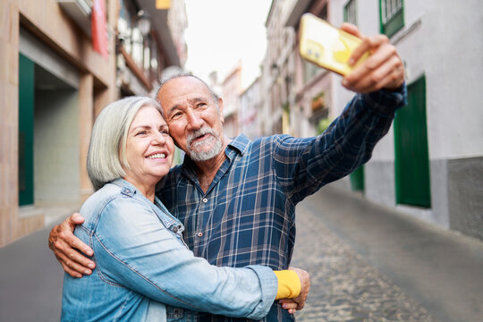 Happy senior couple taking selfie with mobile phone outdoor - Elderly tourist and travel vacations - Focus on faces