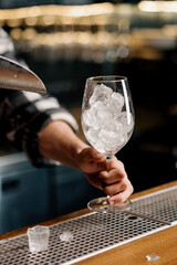 Professional bartender pours ice cubes with a scoop into a glass Process of making cold cocktails Summer fun at the bar