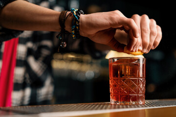 bartender squeezing a piece of orange peel and garnishing a negroni cocktail at the bar close-up