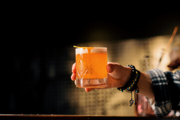 A close-up of a bar guest holding a ready-made tasty peach sour alcoholic cocktail in his hand