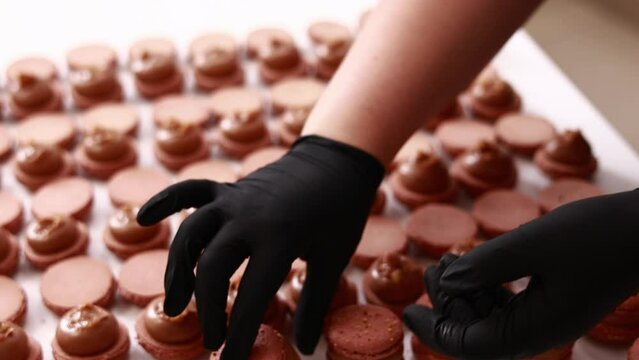 Process of making macarons macaroons, french dessert. chef hands in black gloves are assembling, connecting of two halves with chocolate stuffing at pastry shop. cooking, food and baking concept