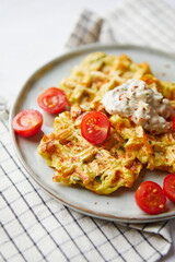 Snack waffles with bacon, cheddar cheese, spinach, sauce and cherry tomatoes on light background