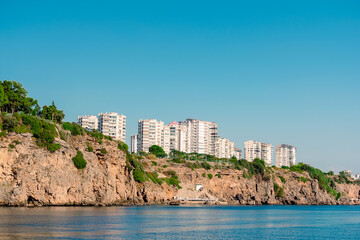 Fototapeta na wymiar View from the sea to a rocky shore with high-rise buildings in the city of Antalya.