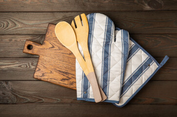 Wooden kitchen utensils, cutting board, potholder and glove on the table, top view. Kitchen Mitten...