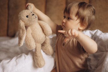 A baby sits on a couch with a stuffed animal.