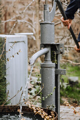 A man, a gardener pumps a hand pump from a metal well in the village, extracting water.