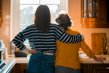 Daughter and her old mother stands near the window and hugs. © Zhanna
