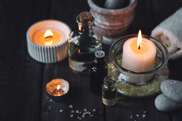 Spa setting with essential oil, candle, sea salt, pebbles, towel on dark wooden background. Massage, aromatherapy. Natural organic ingredients for relaxation, detention. Wellness in salon concept