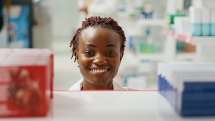 Young pharmacist organizing bottles of pills on racks, putting medicaments and supplements on...