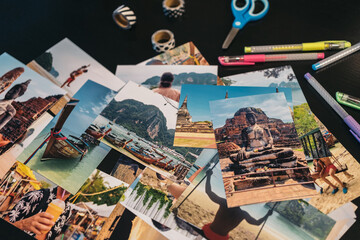 Pile of travel photos on a black table next to a pair of scissors and several rolls of washi tape.