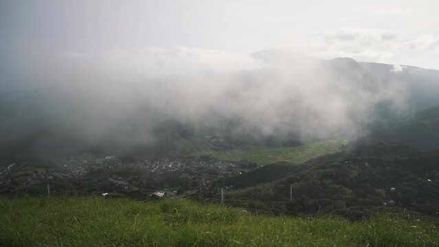 Mist in the green mountains of Japan with a village in the valley below