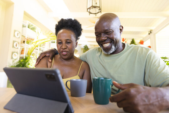 Happy senior african american couple using tablet with cups of coffee
