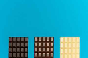 Half bars of dark, milk and white chocolate on a blue background. High quality photo