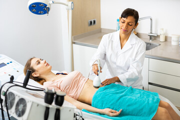 Obraz premium Hispanic woman cosmetologist using equipment for ultrasound lifting procedure for caucasian woman.