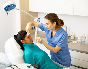 Skilled female beautician with pencil and ruler giving consultation to woman patient in aesthetic...