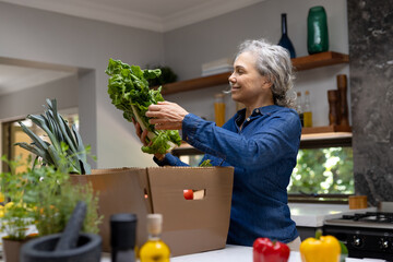 Happy senior caucasian woman unpacking groceries in kitchen