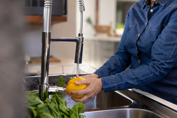 Midsection of senior caucasian woman washing pepper in kitchen