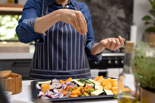 Midsection of senior caucasian woman seasoning vegetables in kitchen