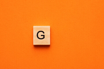 Alphabet capital letter G on wooden square tile - Orange foamy background