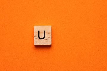 Alphabet capital letter U on wooden square tile - Orange foamy background