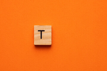 Alphabet letter T on wooden square tile - Orange foamy background