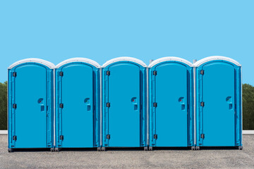 A group of outdoor portable outhouse public toilets with a blue background
