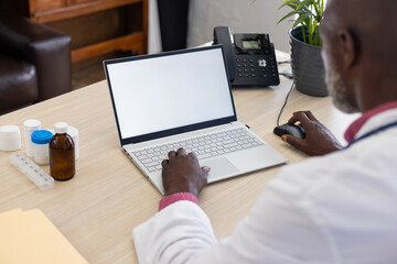 African american male doctor using laptop with copy space on screen at doctor's office