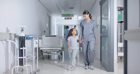 Diverse female nurse and child patient walking through corridor at hospital, in slow motion