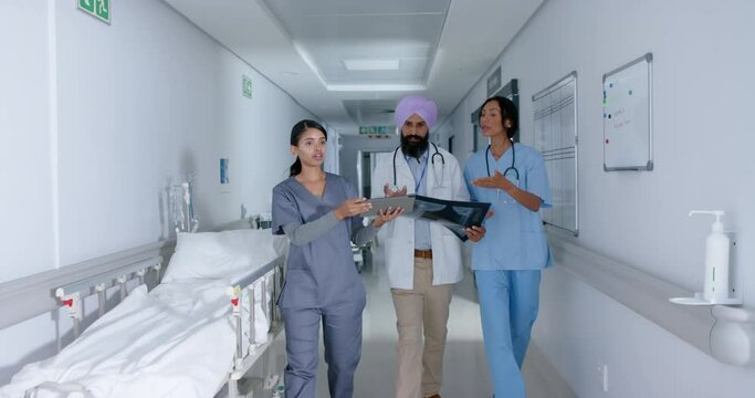 Diverse doctors and nurse using tablet and walking through corridor at hospital, in slow motion