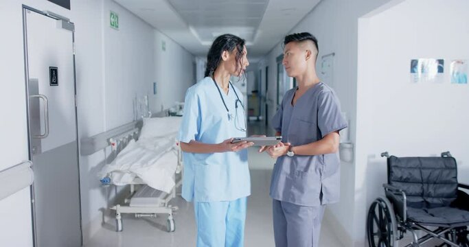 Diverse doctor and nurse using tablet and talking in corridor at hospital, in slow motion