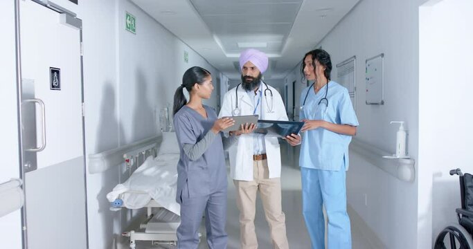Diverse doctors and nurse using tablet and walking through corridor at hospital, in slow motion