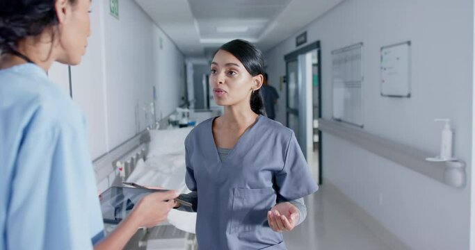 Diverse doctor and nurse using tablets and talking in corridor at hospital, in slow motion