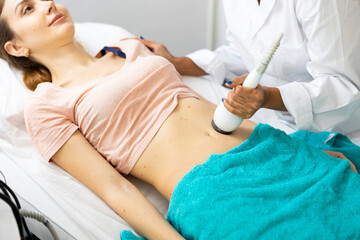 European woman having cavitation procedure removing cellulite on abdomen in modern beauty clinic