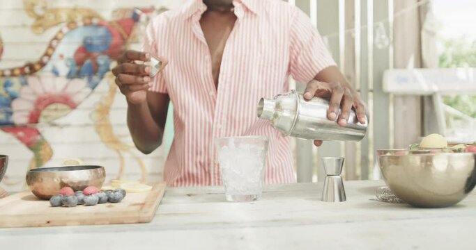 Midsection of african american barman pouring cocktail behind the counter at beach bar, slow motion