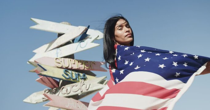 Happy hispanic woman dancing with american flag by signpost on sunny beach, slow motion