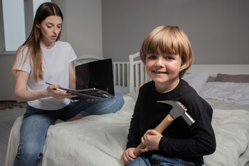 A happy but disobedient child broke his mother's computer with a hammer. Mom is shocked that her son broke her computer. Naughty boy. The kid upset his mother. Toddler want mother's attention.
