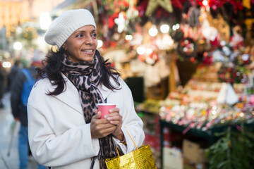 Latin woman with paper cup of hot drink walking at christmas fair.