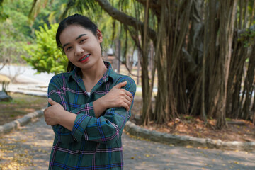 Woman embrace concept.She is wearing braces. Asian woman in green plaid shirt embracing herself happily in the park  looking at the camera and smiling