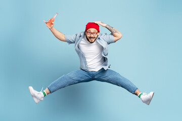 Fototapeta na wymiar Overjoyed asian man wearing red hat, holding bottle with drink jumping high, having fun isolated on blue background. Freedom, emotions, positive lifestyle concept
