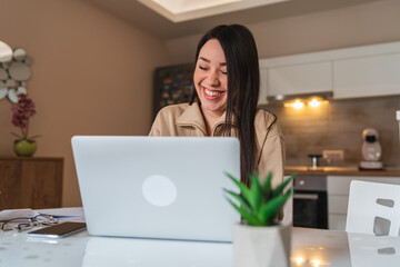 A young woman is working from her kitchen using laptop drinking coffee and using mobile phone