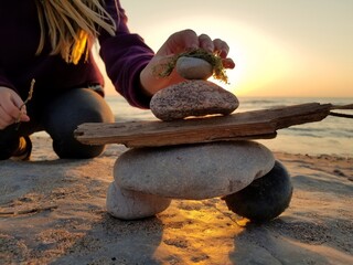 A young girl puts the final rock on an inuksuk inukshuk she's built at the beach at sunset 2 - obrazy, fototapety, plakaty