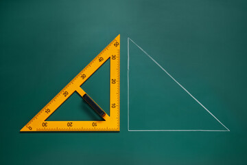 Ruler and triangle drawn with chalk on green board, top view
