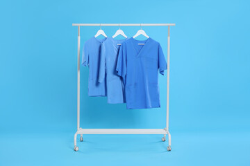 Medical uniforms on rack against light blue background