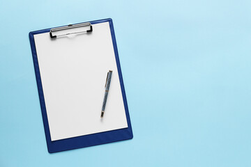 Ballpoint pen and clipboard with paper sheet on light blue background, top view. Space for text
