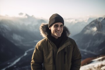 Fototapeta na wymiar Handsome young man in winter jacket and hat standing on top of a mountain and smiling