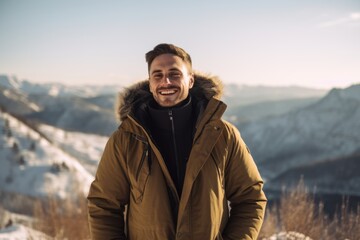 Handsome young man in winter jacket smiling and looking away while standing on top of a mountain