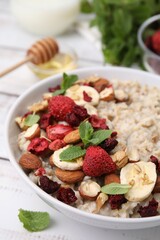 Delicious oatmeal with freeze dried berries, banana, nuts and mint on white table, closeup