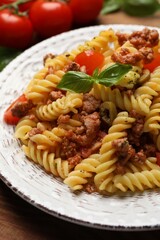 Plate of delicious pasta with minced meat, tomatoes and basil on table, closeup