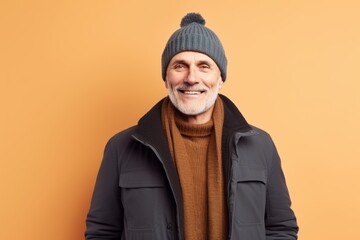 Fototapeta premium smiling senior man in winter clothes and hat looking at camera isolated on orange